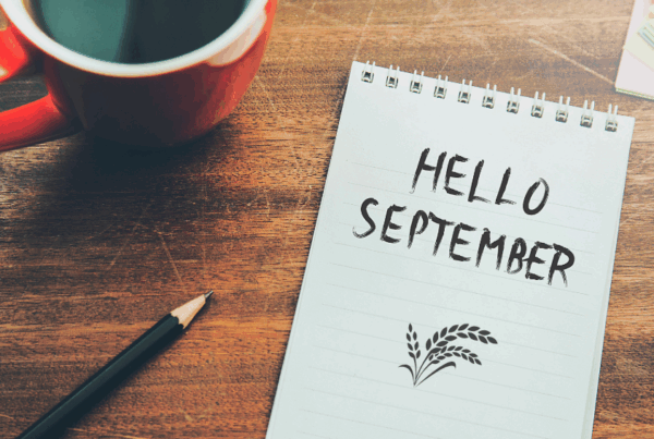 Coffee cup on a table with note pad and drawing pencil with "Hello September" drawn on the paper